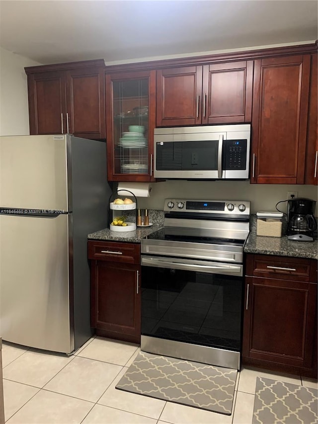 kitchen featuring light tile patterned floors, stainless steel appliances, and dark stone counters