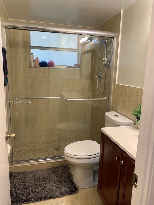 bathroom with tile patterned floors, an enclosed shower, vanity, tile walls, and toilet