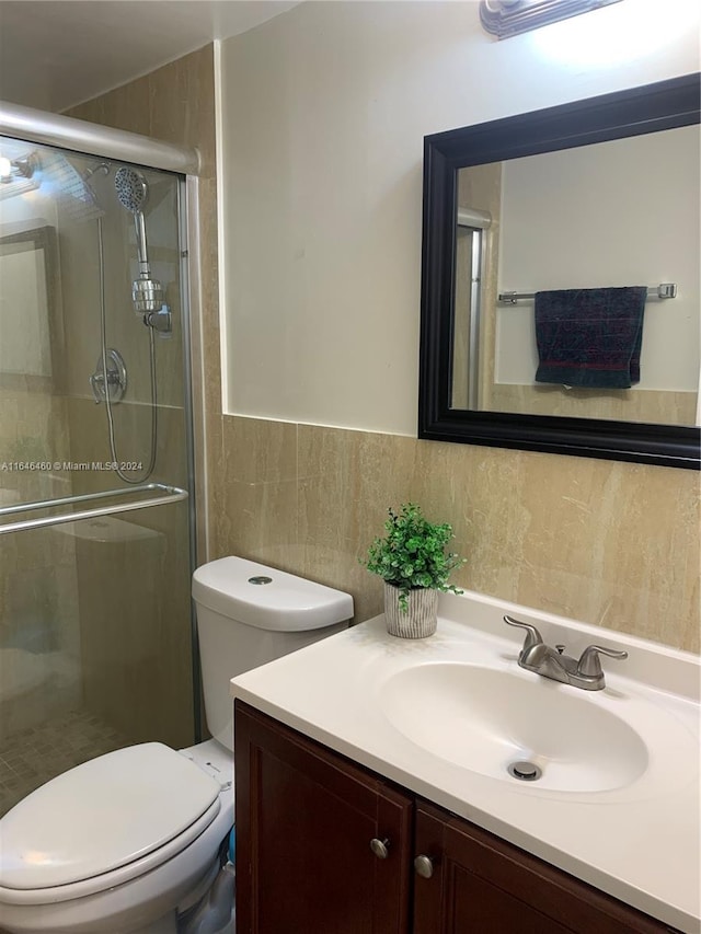 bathroom with vanity, toilet, a shower with door, and tile walls