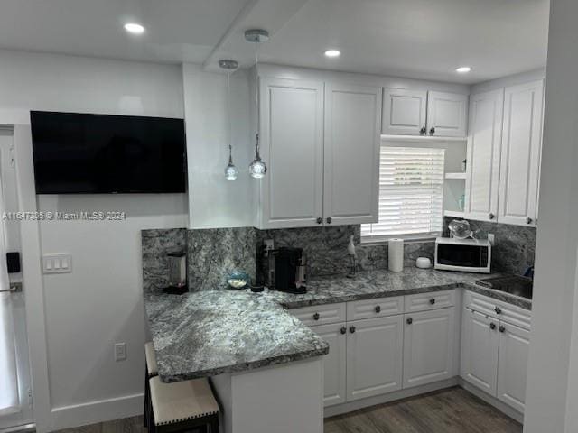 kitchen with white cabinetry, backsplash, hardwood / wood-style flooring, and kitchen peninsula