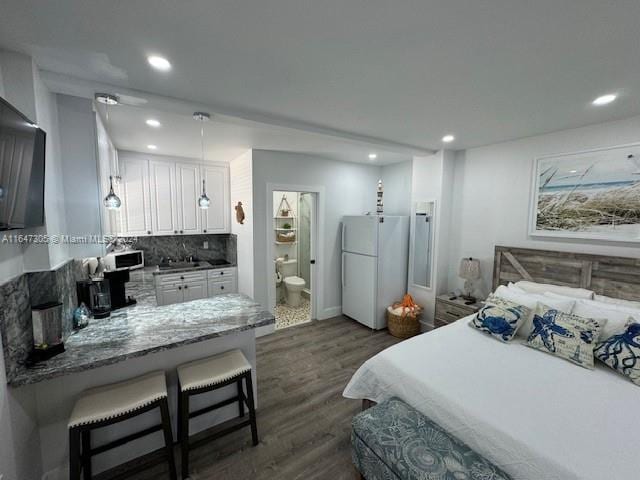 bedroom featuring sink, ensuite bathroom, white refrigerator, and dark hardwood / wood-style floors