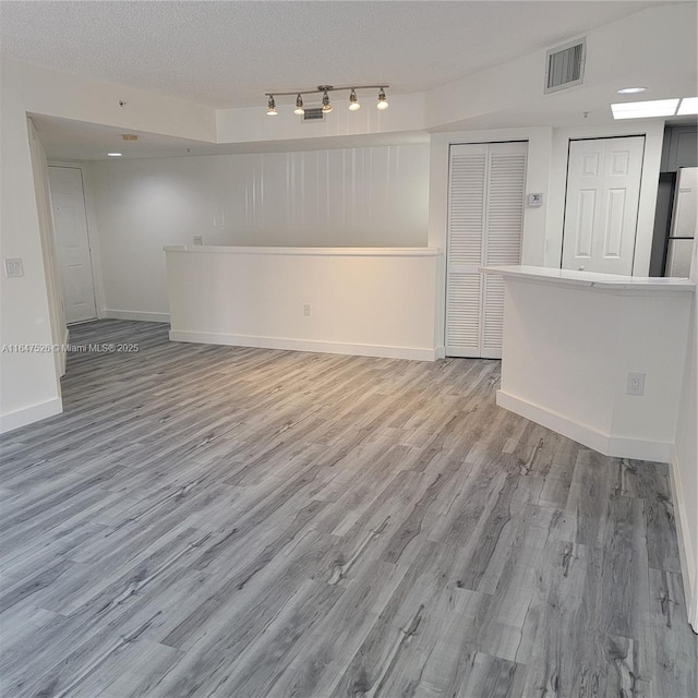 unfurnished room with a textured ceiling, light wood-type flooring, visible vents, and baseboards