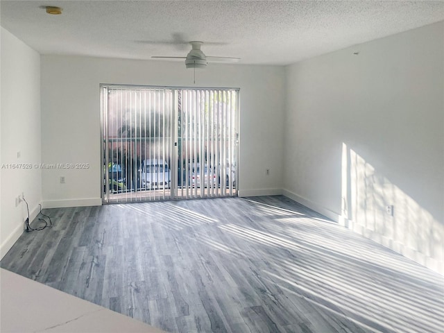 empty room featuring a textured ceiling, wood finished floors, and baseboards