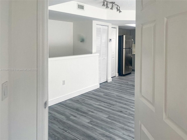 hall featuring a textured ceiling, dark wood-style flooring, visible vents, baseboards, and rail lighting