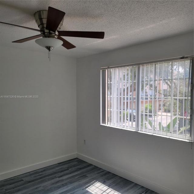 spare room with a textured ceiling, dark wood-style flooring, and baseboards