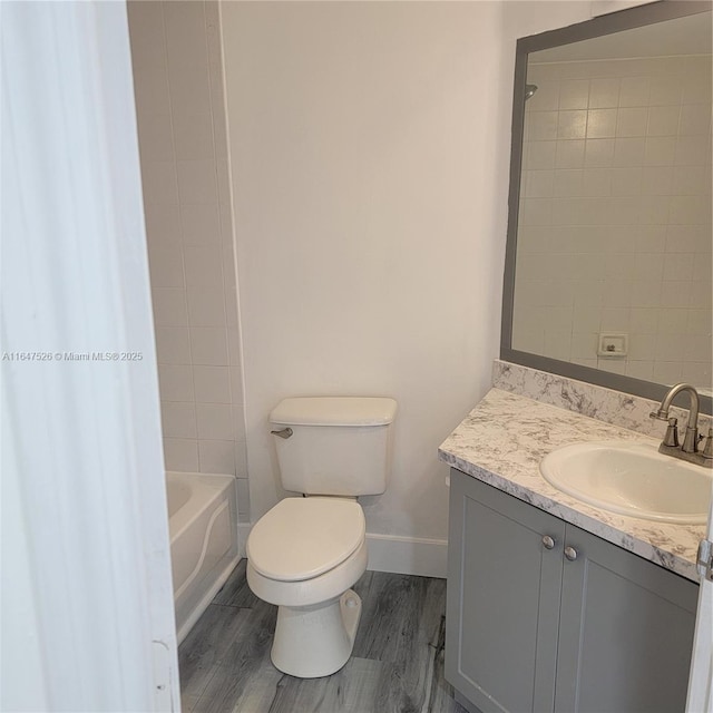 bathroom featuring baseboards, toilet, wood finished floors, vanity, and washtub / shower combination