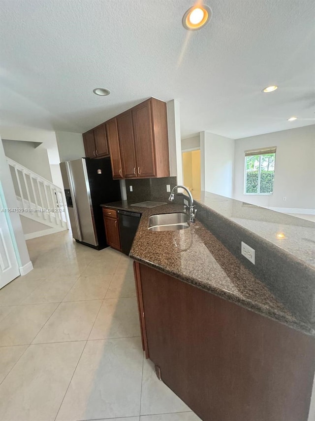 kitchen with dark stone counters, stainless steel fridge, kitchen peninsula, sink, and black dishwasher