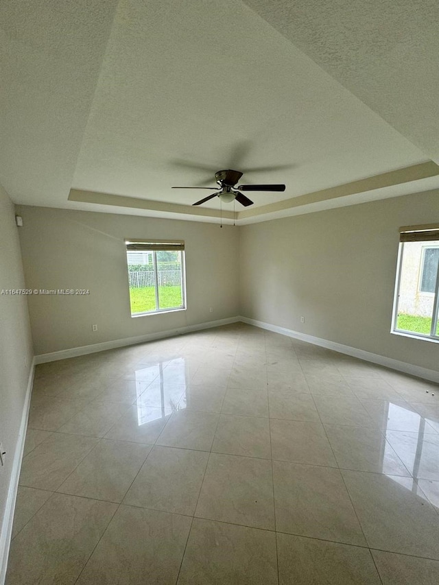 empty room with a textured ceiling, ceiling fan, light tile patterned floors, and a tray ceiling