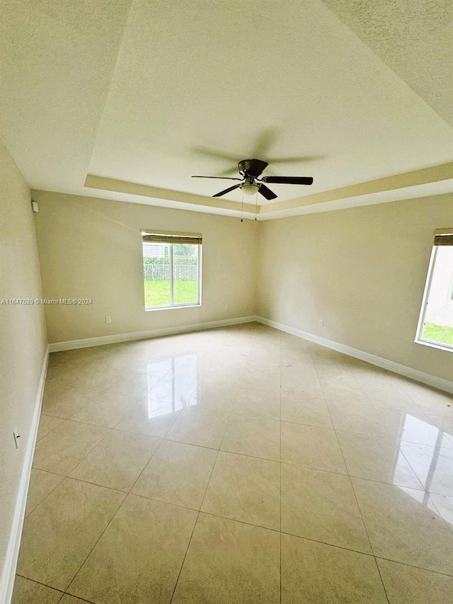 unfurnished room with a wealth of natural light, a raised ceiling, ceiling fan, and a textured ceiling