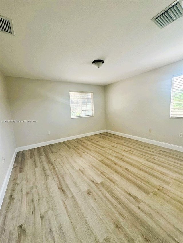 unfurnished room with a textured ceiling and light hardwood / wood-style floors