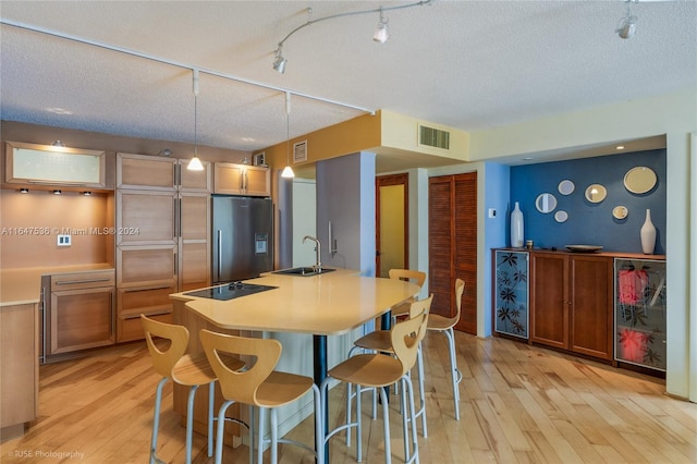 kitchen featuring sink, black electric stovetop, light hardwood / wood-style floors, a textured ceiling, and refrigerator with ice dispenser