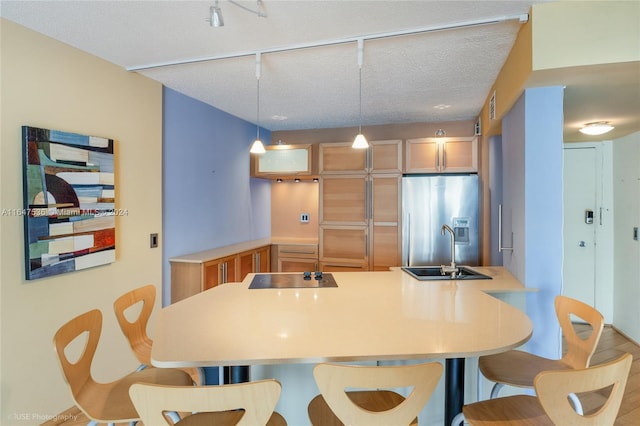 kitchen featuring rail lighting, sink, a textured ceiling, stainless steel fridge with ice dispenser, and kitchen peninsula