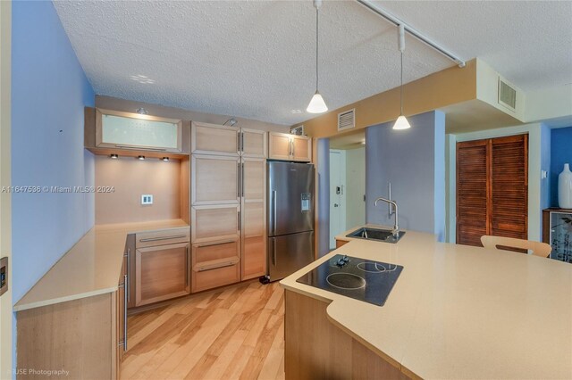 kitchen with black electric stovetop, light hardwood / wood-style flooring, pendant lighting, stainless steel refrigerator with ice dispenser, and sink