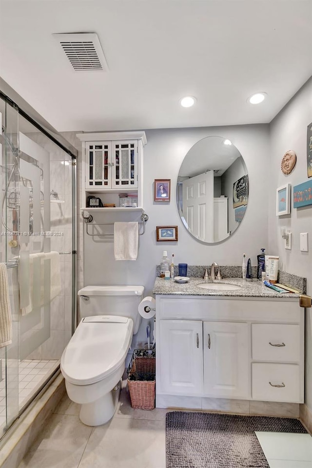 bathroom with a shower with shower door, toilet, vanity, and tile patterned floors