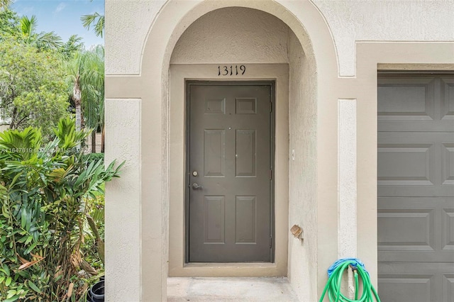 doorway to property with a garage and stucco siding