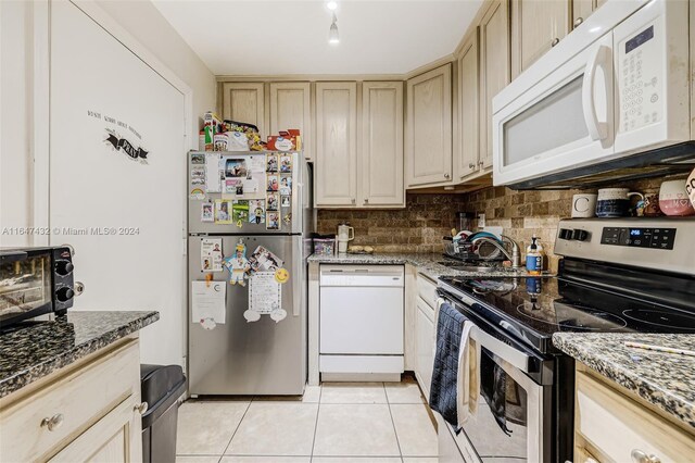 kitchen featuring light tile patterned floors, backsplash, stainless steel appliances, and dark stone counters