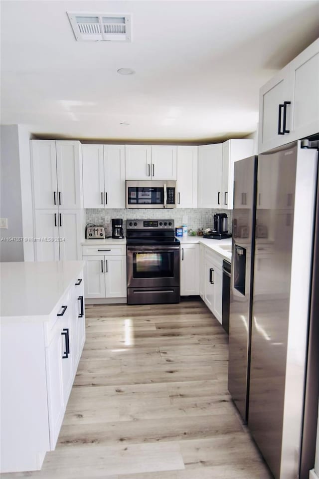 kitchen featuring decorative backsplash, white cabinetry, light hardwood / wood-style flooring, and appliances with stainless steel finishes