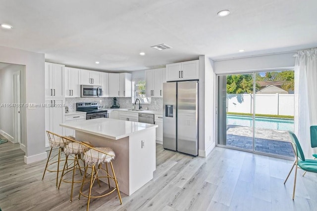 kitchen with appliances with stainless steel finishes, a kitchen breakfast bar, sink, white cabinets, and a kitchen island