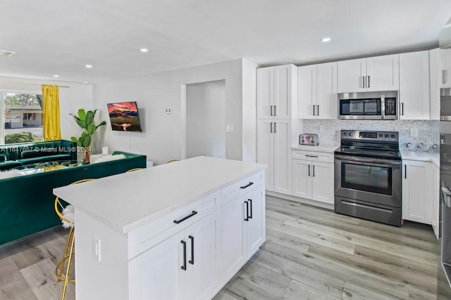 kitchen with white cabinets, stainless steel appliances, a kitchen island, and light hardwood / wood-style flooring