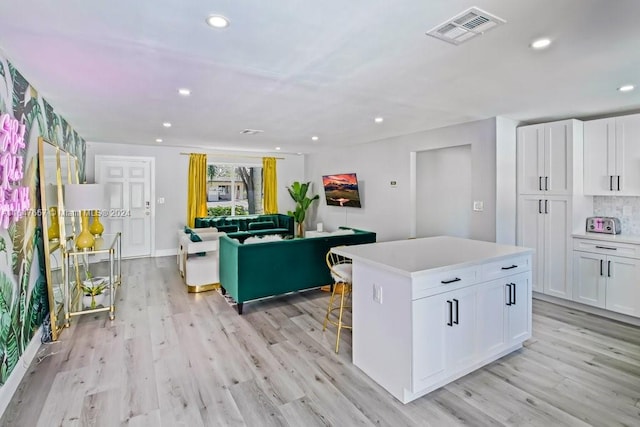 kitchen with tasteful backsplash, light hardwood / wood-style flooring, white cabinets, and a kitchen island