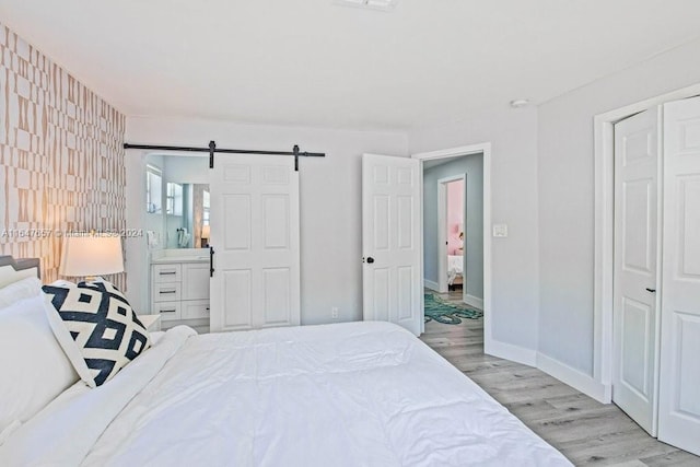 bedroom featuring a barn door, light hardwood / wood-style floors, and connected bathroom