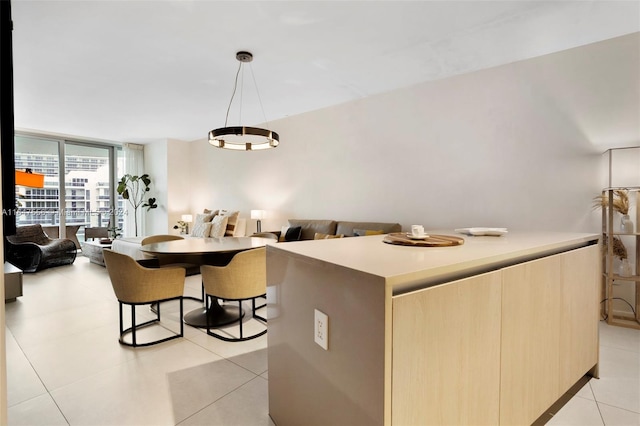 kitchen with a center island, a wall of windows, light brown cabinets, light tile patterned flooring, and pendant lighting