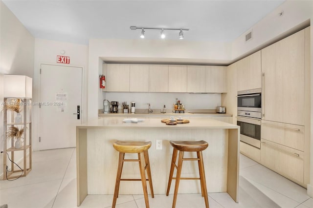 kitchen with track lighting, a kitchen bar, a center island, double oven, and light tile patterned flooring