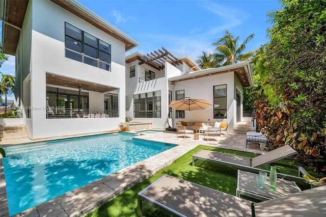 rear view of property with a patio, a balcony, an outdoor pool, and stucco siding