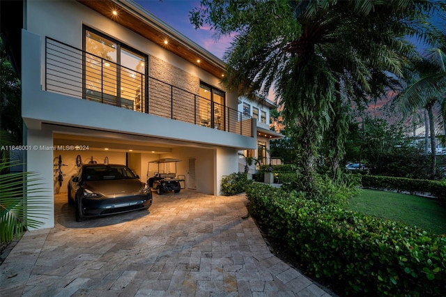 back house at dusk with a balcony, a lawn, and a garage