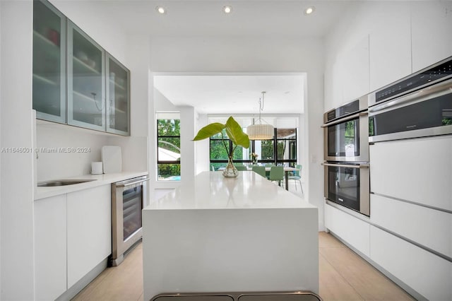 kitchen with light hardwood / wood-style flooring, white cabinetry, wine cooler, double oven, and a center island