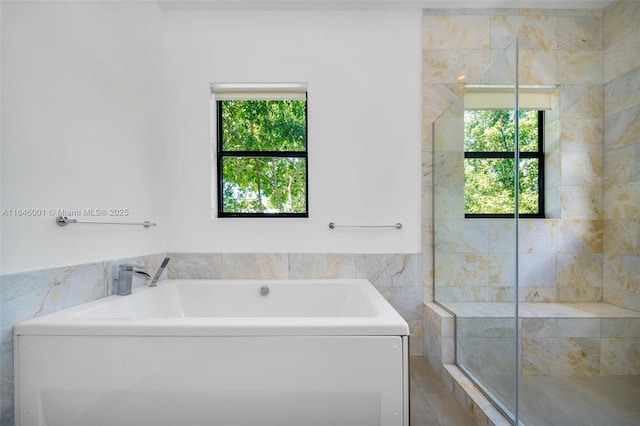 full bath with tile walls, a garden tub, a healthy amount of sunlight, and a tile shower