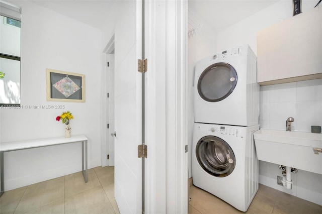 laundry area featuring light tile patterned floors, stacked washer and clothes dryer, laundry area, and a sink