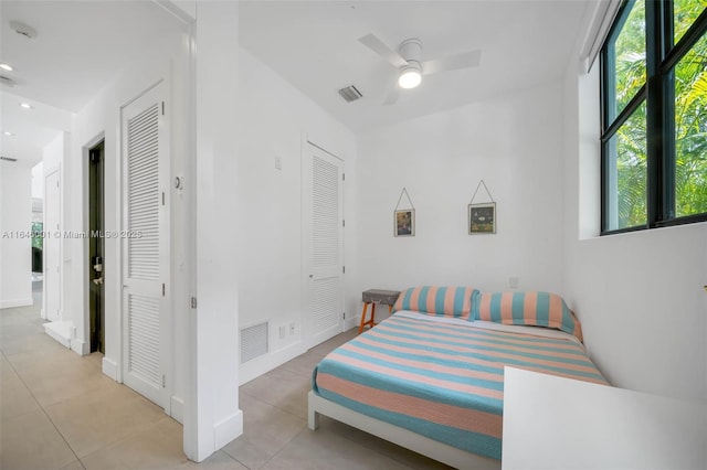 bedroom with light tile patterned floors, a ceiling fan, visible vents, and multiple closets