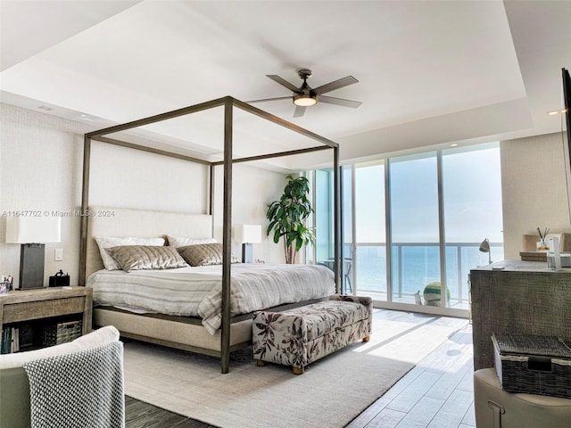 bedroom featuring hardwood / wood-style flooring, access to outside, ceiling fan, a water view, and floor to ceiling windows