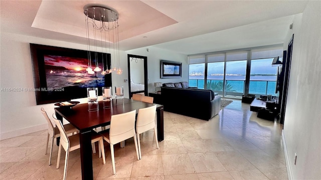 tiled dining space with a tray ceiling, expansive windows, a water view, and an inviting chandelier