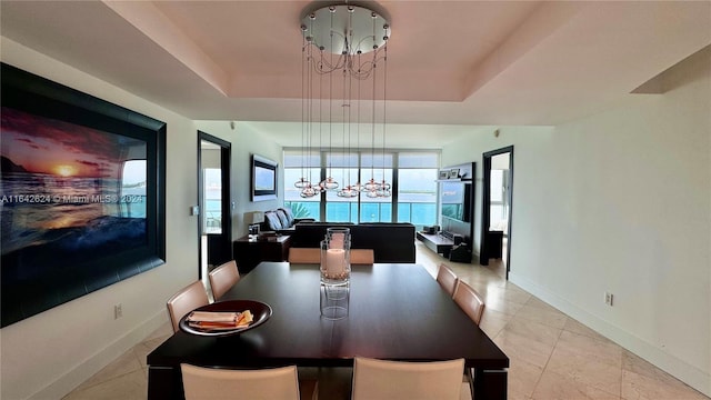 dining space with a tray ceiling, a notable chandelier, and light tile patterned floors