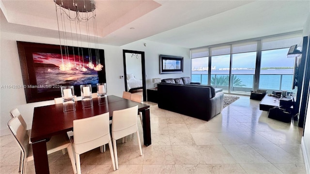 dining area with a notable chandelier, a water view, expansive windows, a tray ceiling, and light tile patterned floors