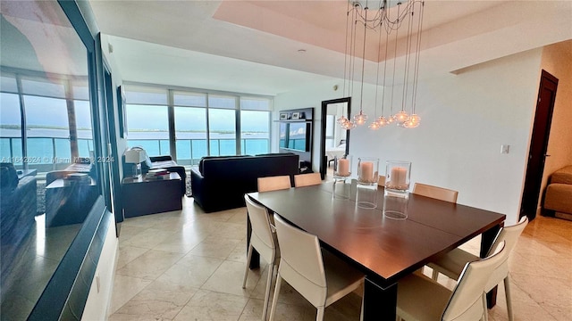 tiled dining space with a raised ceiling, a notable chandelier, floor to ceiling windows, and a water view