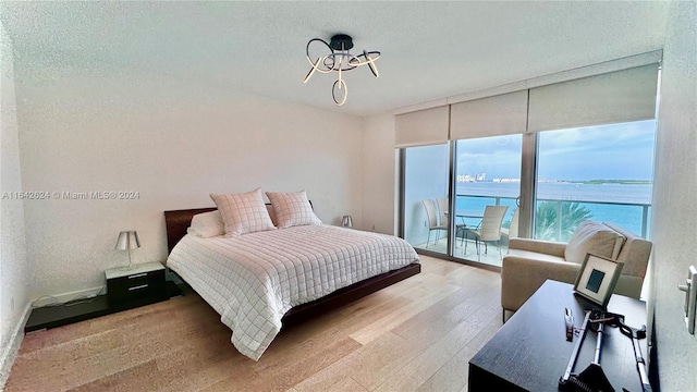 bedroom featuring a textured ceiling, light hardwood / wood-style flooring, a water view, and access to outside