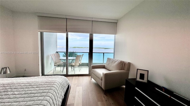 bedroom with light hardwood / wood-style flooring, access to exterior, and a water view