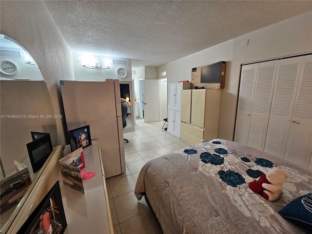 bedroom with a closet, a textured ceiling, light tile patterned flooring, and fridge