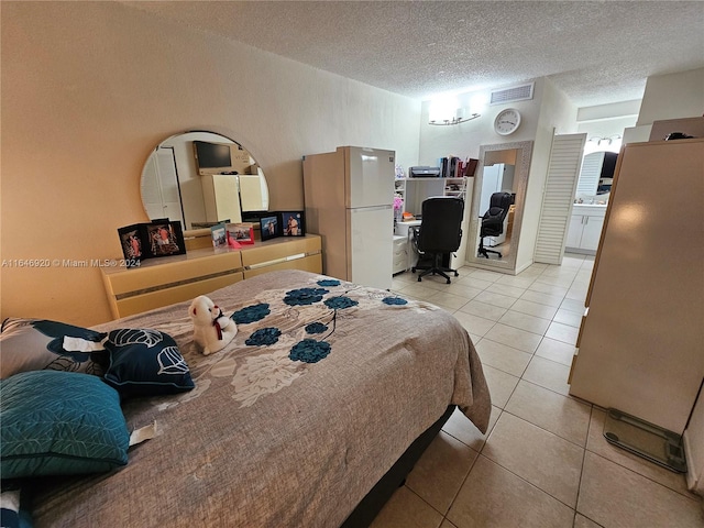 bedroom with a textured ceiling, white refrigerator, ensuite bathroom, and light tile patterned floors