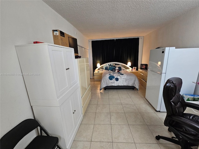 bedroom with a textured ceiling, light tile patterned floors, and white fridge