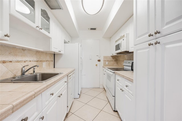 kitchen featuring light tile patterned floors, decorative backsplash, white cabinets, a sink, and white appliances