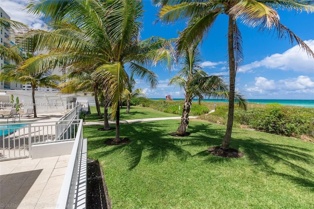 view of community with a pool, a water view, a lawn, and a beach view