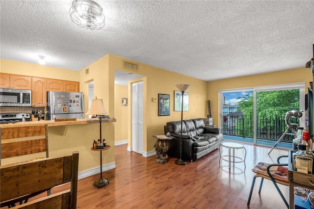 living room featuring visible vents, a textured ceiling, baseboards, and wood finished floors