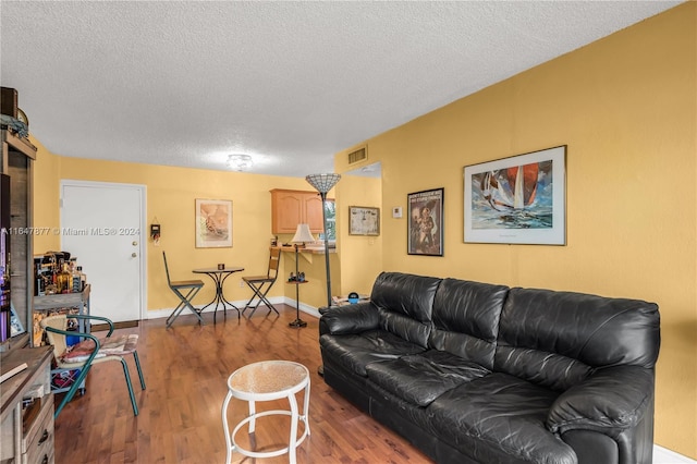 living room featuring visible vents, baseboards, a textured ceiling, and wood finished floors