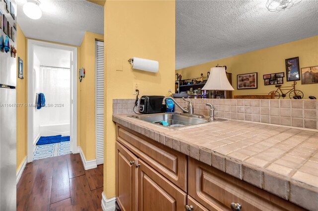 kitchen with sink, a textured ceiling, tile counters, and wood-type flooring