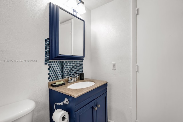 half bath with backsplash, toilet, and vanity