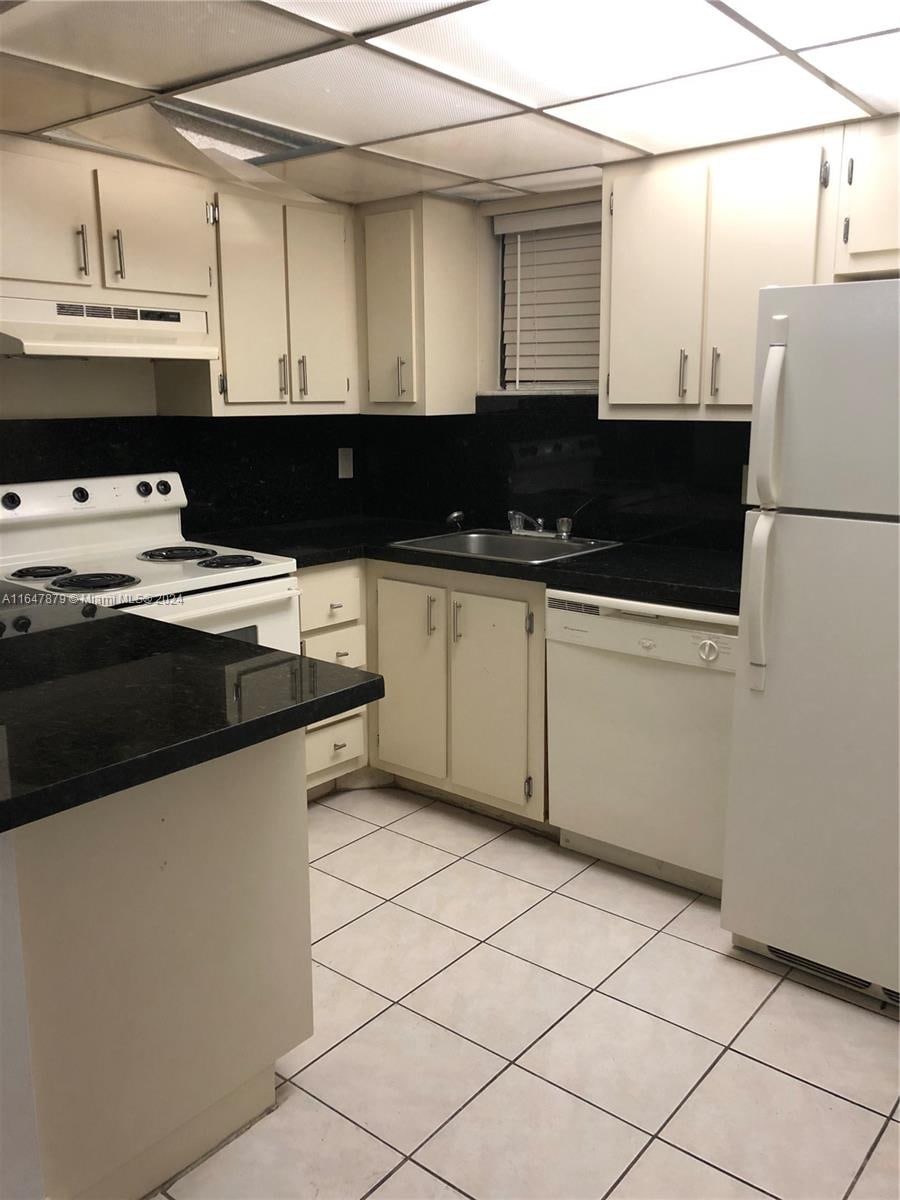 kitchen featuring backsplash, a paneled ceiling, light tile patterned floors, sink, and white appliances